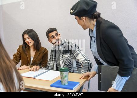 Étudiants universitaires collaborant à un bureau, s'engageant dans des sessions d'étude tout en recevant des conseils de leur professeur dans un cadre de classe dynamique Banque D'Images