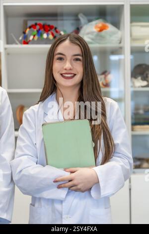 Portrait d’une étudiante en médecine souriante tenant un dossier dans un laboratoire universitaire, mettant en valeur son dévouement à l’éducation en santé Banque D'Images