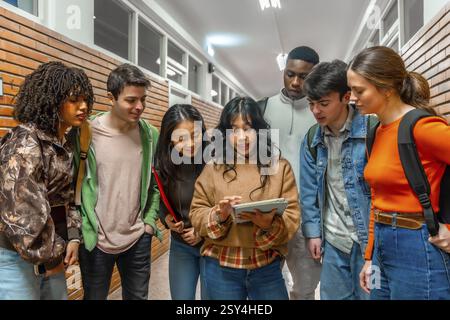 Groupe diversifié d'étudiants collégiaux collaborant sur un projet, en utilisant une tablette numérique dans un couloir universitaire Banque D'Images
