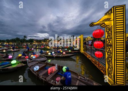 Touristes sur un pont piétonnier à Hoi an, Hội an et de nombreux bateaux avec des lanternes lors d'une croisière en soirée sur la rivière Thu bon, Sông Thu Bồn. Banque D'Images