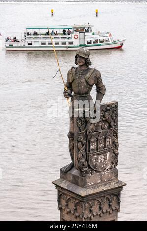 Prague, République tchèque - 12 juin 2016 : une statue d'un chevalier tenant une lance se dresse bien en vue près de la rivière Vltava, avec un bateau d'excursion passant dans le b Banque D'Images