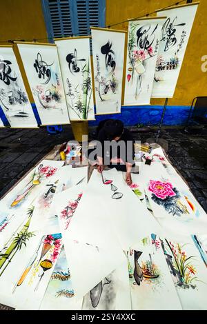 Un artiste peint des tableaux colorés avec des caractères chinois anciens sur un sentier à Hoi an, Hái an. Province de Hoi an Quang Nam Vietnam FB 2024 4232 Banque D'Images