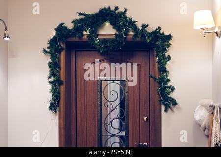 La porte d'entrée est décorée avec une branche d'arbre de Noël avec une guirlande LED sur un fil. Décorations festives comme symbole de Noël qui approche. Photo de haute qualité Banque D'Images