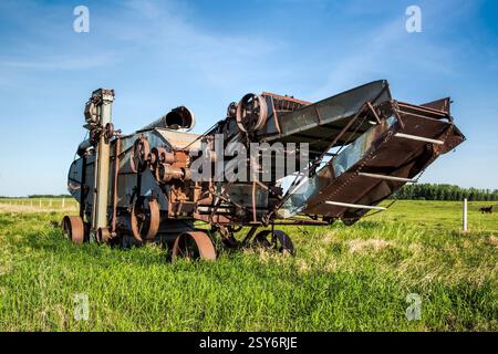 Une grande machine rouillée est assise dans un champ. La machine est une moissonneuse-batteuse Banque D'Images