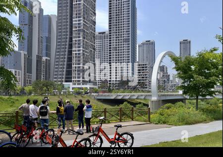 Sejong City, Corée du Sud - 26 mai 2021 : un groupe de cyclistes s'arrête le long d'un chemin au bord de la rivière pour admirer l'horizon moderne de Sejong City, avec le disti Banque D'Images