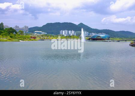 Sejong City, Corée du Sud - 26 mai 2021 : une fontaine jaillit dans le lac artificiel du parc du lac Sejong, avec un pavillon flottant futuriste et des pedes Banque D'Images