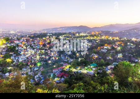 Vue sur la ville de Cebu City, Philippines au crépuscule avec des lumières de la ville illuminant les maisons résidentielles, les bâtiments et les structures à flanc de colline Banque D'Images