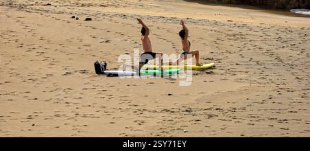 Séance de yoga en plein air, deux personnes pratiquent sur des planches de surf sur une plage, Piedra Playa, Fuerteventura, Îles Canaries, Espagne. Prise 2024 Banque D'Images