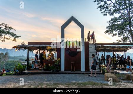 Krabi, Thaïlande - 23 déc. 2024 : le café animé propose des personnes qui se socialisent par une chaude soirée, entouré d'une végétation luxuriante et d'un magnifique coucher de soleil Banque D'Images