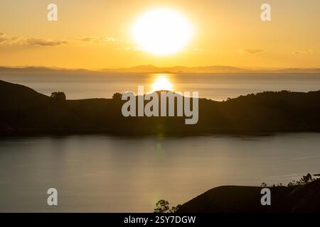 Coucher de soleil paisible sur le lac Titicaca vu de l'île du soleil, projetant des teintes chaudes sur l'eau tranquille en contrebas Banque D'Images