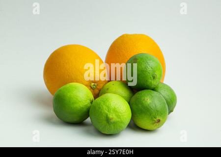 Cette image présente un groupe d'agrumes, y compris des oranges et des citrons verts. Il y a deux oranges entières, dont l'une a été coupée en deux pour la révéler Banque D'Images