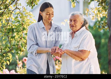 Se tenant la main. La jeune femme est avec sa mère aînée est dans le jardin. Banque D'Images