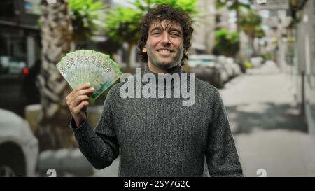 Homme hispanique tenant des roubles russes sur une rue de la ville à l'extérieur, mettant en valeur la monnaie dans un environnement urbain sous la lumière du jour naturelle. Banque D'Images