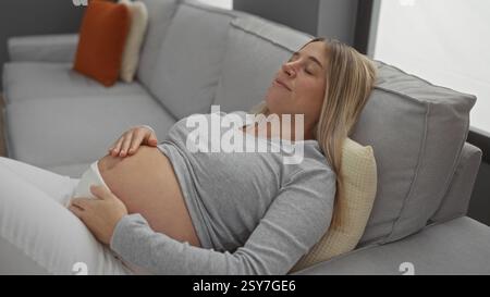 Femme enceinte se relaxant sur un canapé confortable dans un salon confortable, posant doucement ses mains sur son ventre tout en attendant un bébé dans une maison paisible Banque D'Images
