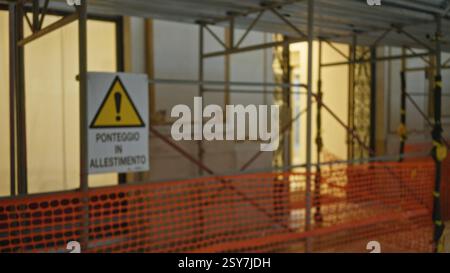 Chantier de construction flou avec échafaudage et panneau d'avertissement en italien illustrant une vue défocalisée d'une zone de construction urbaine en rénovation. Banque D'Images
