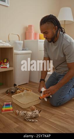 Jeune homme avec des tresses s'agenouille dans un salon confortable organisant des jouets, soulignant un environnement familial organisé et paisible. Banque D'Images