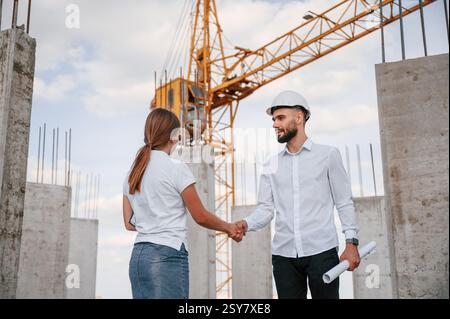Établissement de la poignée de main. Accord réussi. Homme en uniforme travaillant avec la femme sur le chantier de construction. Banque D'Images
