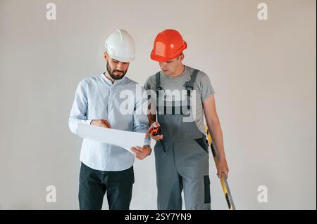 Debout et lisant le plan. Deux hommes font des réparations dans l'appartement ensemble. Banque D'Images