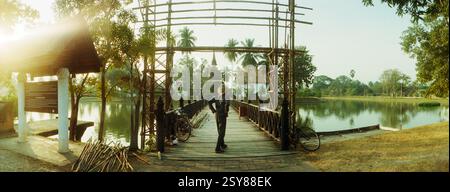 Vue panoramique de l'homme reconstruisant l'entrée d'un pont en bois menant à un temple bouddhiste, parc historique de Sukhothai, Sukhothai, Thaïlande Banque D'Images