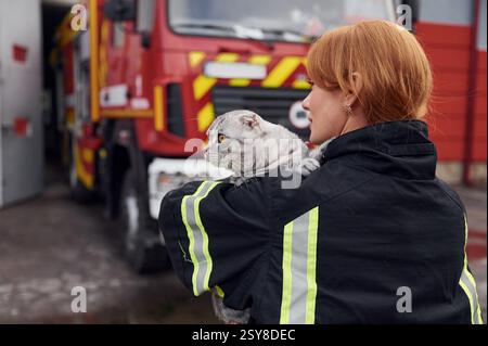Vue de derrière. Tenant le chat sur les épaules. Une femme pompière en uniforme est au travail dans le département. Banque D'Images