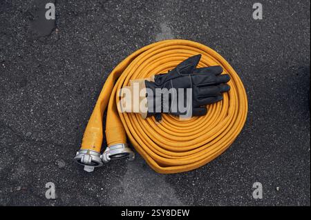 Vue de dessus du tuyau d'incendie jaune avec des gants noirs sur elle au sol. Banque D'Images