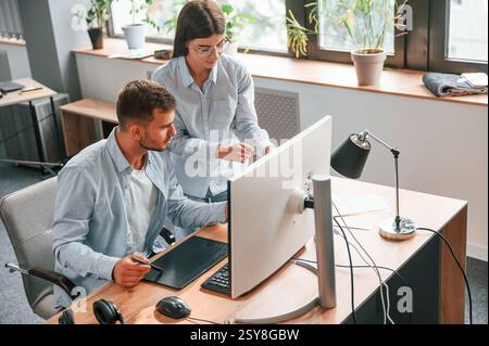 L'homme est assis, la femme est debout. À l'aide d'un pc. Deux jeunes designers travaillent ensemble au bureau. Banque D'Images