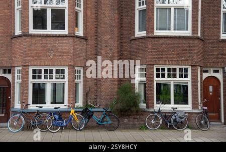 Vélos colorés garés sur le trottoir devant un bâtiment en brique hollandais typique avec des fenêtres blanches Banque D'Images