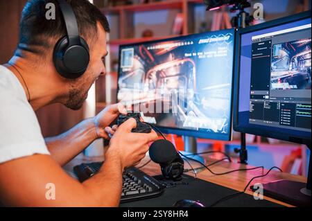 Jouer à un jeu de tir à la première personne. Streamer masculin dans des vêtements décontractés est à l'intérieur avec pc. Banque D'Images