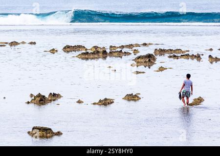 Homme pataugant dans l'eau peu profonde près d'une plage rocheuse sur l'île de Siargao Philippines Banque D'Images