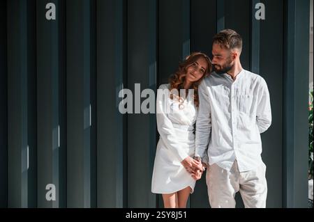 Se tenir debout et se tenir les uns les autres par les mains. Beau jeune couple est debout ensemble sur fond vert foncé. Banque D'Images