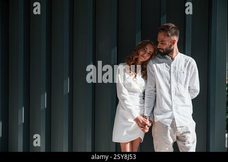 Se tenir debout et se tenir les uns les autres par les mains. Beau jeune couple est debout ensemble sur fond vert foncé. Banque D'Images