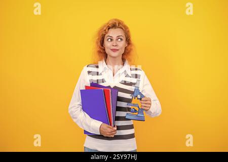 La recherche microscopique. Une femme professeur de biologie scolaire tient un microscope. Femme professeur de biologie. Retour à l'école. Professeur avec microscope sur jaune Banque D'Images
