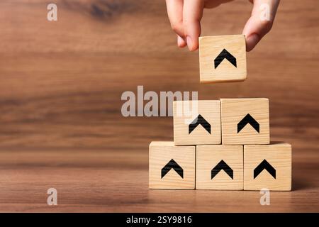 Femme empilant des cubes en bois avec des flèches noires sur fond en bois, gros plan. Espace pour le texte Banque D'Images