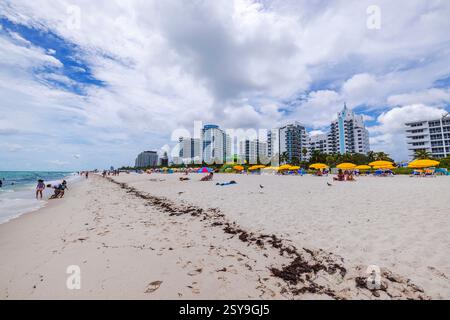 Plage de sable avec des parasols jaunes et des gratte-ciel modernes sur Miami Beach contre le ciel bleu avec des nuages blancs. Miami Beach. ÉTATS-UNIS. Banque D'Images