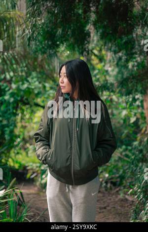 Jeune femme debout sur un chemin de jardin verdoyant dans des vêtements décontractés, entourée de verdure douce et de lumière naturelle filtrée. Golden Gate Park Banque D'Images
