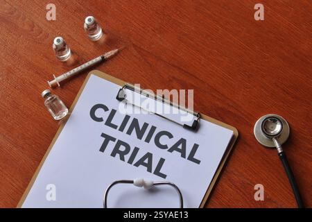 Une presse-papiers avec les mots « CLINICAL TRIAL » sur une table en bois avec une seringue, des flacons et un stéthoscope. Concept médical et de santé. Banque D'Images
