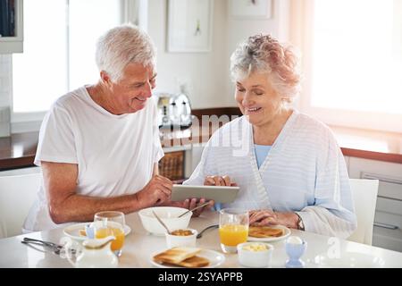 Sourire, couple senior et tablette dans la cuisine sur les médias sociaux, lire blog et recherche sur Internet. Personnes âgées, application numérique et liaison pour le petit déjeuner Banque D'Images
