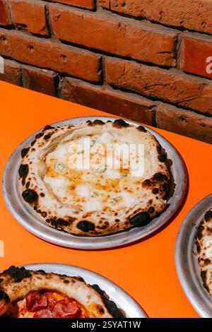Pizza aux quatre fromages fraîchement préparée avec parmesan, mozzarella et dorblu sur une croûte croustillante, servie sur un plateau en métal sur un ta orange vif Banque D'Images