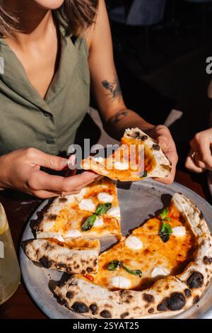 Une personne tient une tranche de pizza Margherita fraîche garnie de mozzarella et de basilic. La pizza est accompagnée d'une limonade fraîche. Un di extérieur décontracté Banque D'Images