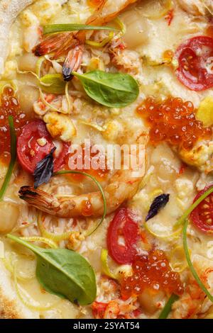 Vue rapprochée d'une délicieuse pizza gastronomique garnie de crevettes succulentes, de caviar rouge vif, de mozzarella crémeuse, de tomates tranchées, d'épinards au basilic, et s. Banque D'Images