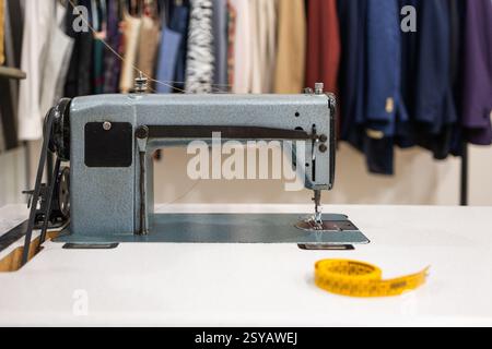 Une machine à coudre vintage se tient sur une table blanche dans un espace de travail, entourée de tissus colorés et d'un ruban à mesurer jaune, incarnant l'essence de Banque D'Images