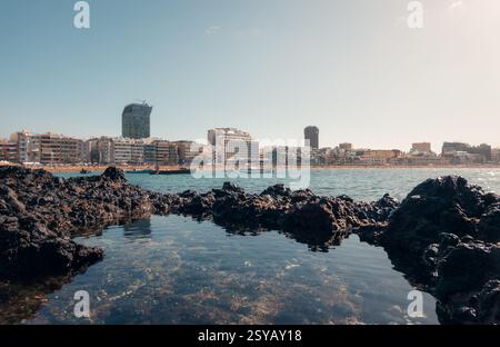 Vue tranquille sur le paysage urbain depuis les roches volcaniques par une journée ensoleillée, montrant des bâtiments modernes et des eaux calmes à Las Palmas, Gran Canaria Banque D'Images