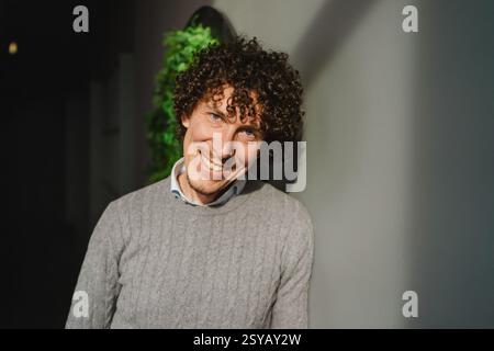 Un jeune homme aux cheveux bouclés se tient devant un mur vert, symbolisant les thèmes de l’écologie et du développement durable. La toile de fond naturelle améliore Banque D'Images