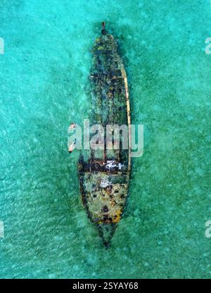Vue aérienne de deux personnes méconnaissables, nagez autour d'un navire coulé couvert de mousse dans les eaux claires et turquoises des Philippines, mettant en évidence un Ser Banque D'Images