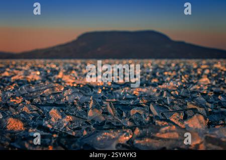 Fonyod, Hongrie - vue panoramique sur le lac Balaton gelé par un après-midi froid d'hiver avec des lumières dorées de coucher de soleil et la montagne Badacsony en arrière-plan Banque D'Images