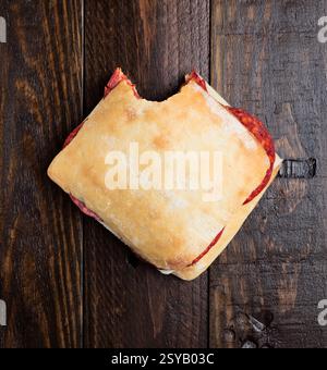 Vue de dessus d'un sandwich au chorizo fait maison avec une bouchée retirée, placé sur une surface en bois rustique. Banque D'Images