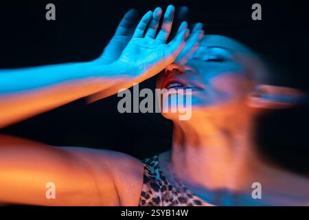 Un portrait dynamique d'une femme chauve utilisant un éclairage créatif et un flou de mouvement. Les teintes bleues et oranges renforcent l'expression artistique et la dép émotionnelle Banque D'Images