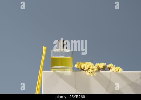 Diffuseur en verre élégant rempli de liquide parfumé au citron, accompagné de bâtonnets jaunes et de fleurs délicates, sur un fond minimaliste. Frais et Banque D'Images