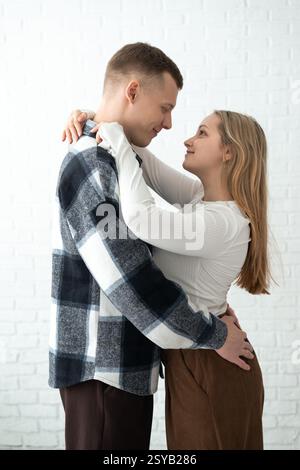 Un couple aimant partage une étreinte chaleureuse dans une pièce très éclairée, véhiculant un sentiment de bonheur et d'intimité. Les deux sourient doucement, appréciant clairement t Banque D'Images
