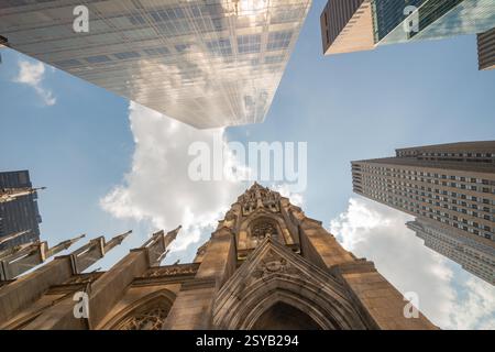 Prise de vue en angle bas capturant l'architecture dynamique de Manhattan avec ses gratte-ciel réfléchissants surplombant la cathédrale historique de Patrick. Banque D'Images